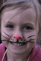 A little girl with face painted like a bunny 