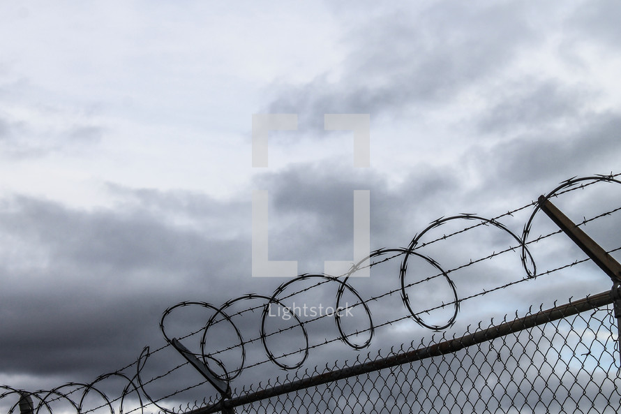 barbed wire at the top of a chain link fence under gray skies