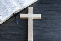 Wood cross laying on a dark wood table by an open bible