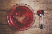 A bowl of red jello with a heart shape spooned out.