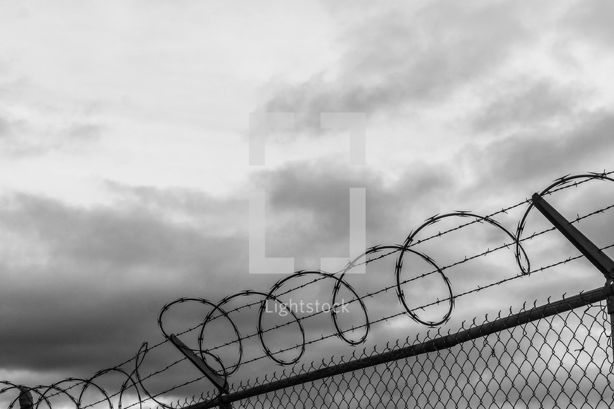 barbed wire on the top of a chain link fence under a gray sky