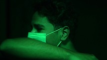face of a man wearing a face mask in green light coughing 