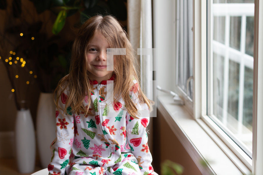 girl in Christmas pajamas sitting in a window 