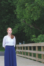 a woman standing on a wood bridge looking out in front of her 