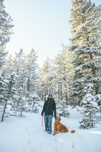 man walking through a snowy forest with his dog 