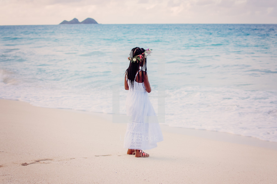 a girl standing on a beach with flowers in her hair 