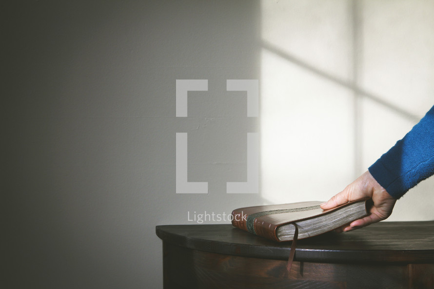 a woman picking up a Bible off a table and cross shadow 