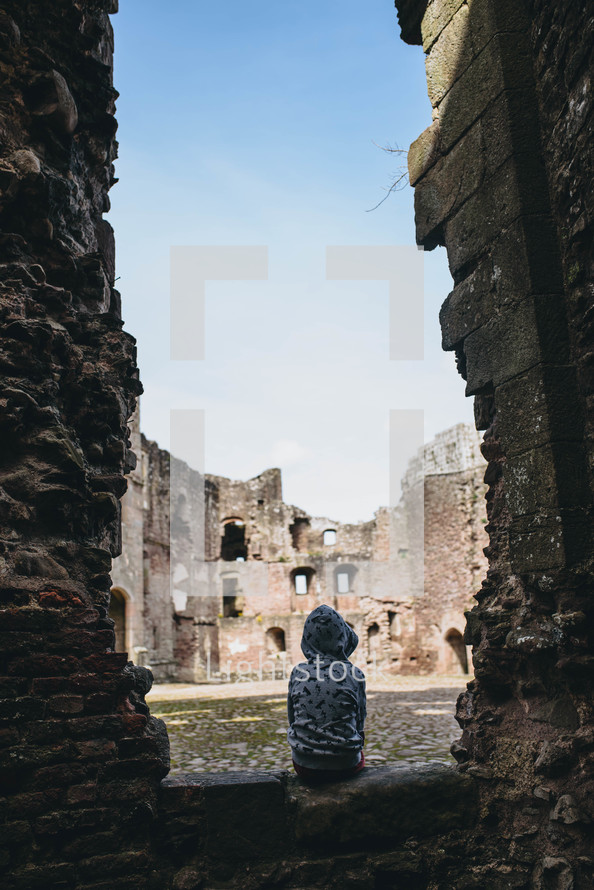 a child sitting in the ruins of a castle 