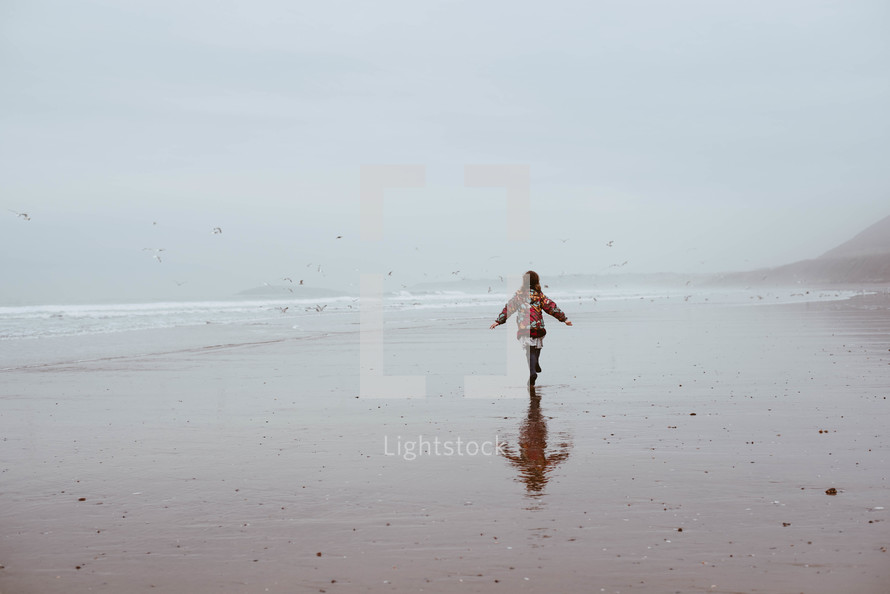 a girl in a coat running on a beach 