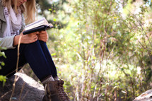 A young woman sits in the woods and reads her Bible.