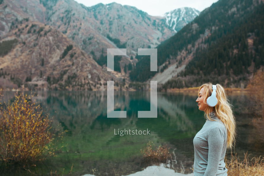 woman listening to headphone by a lake shore 