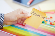 woman holding a sticky note with the word vacation on it 