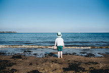 a boy standing on a beach in a bucket hat