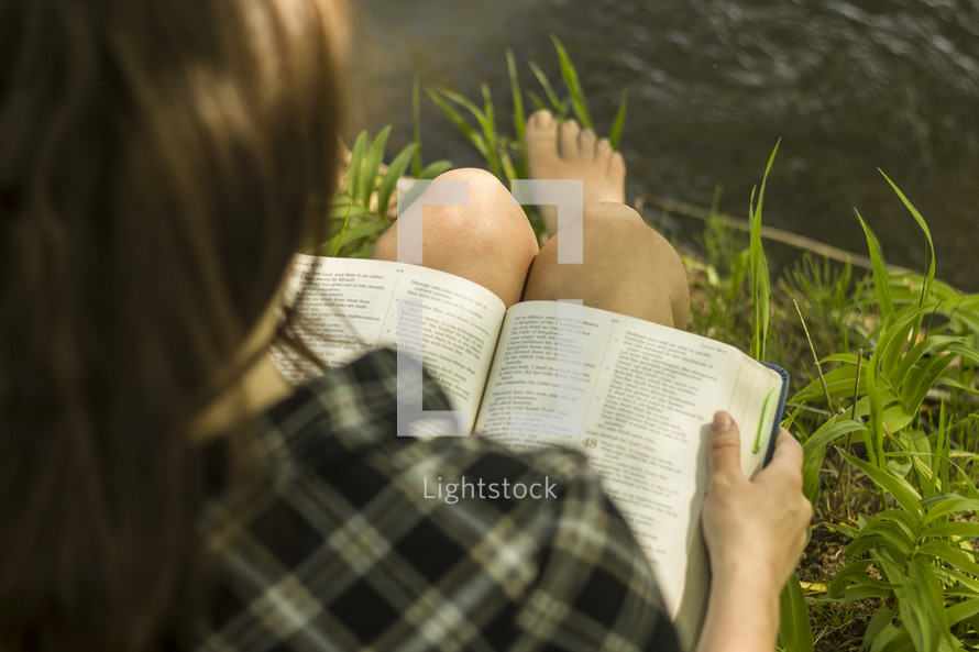 woman reading a Bible by a lake 