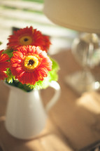 Orange flowers in pitcher on a coffee table.