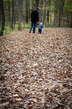 a father and son walking holding hands through fall leaves 