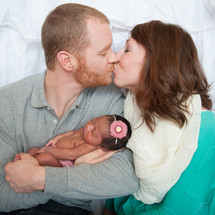 Kissing couple holding a newborn infant.