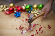 Hand holding a hammer, smashing a glass Christmas ornament on a wooden board.