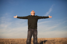 elderly man standing outdoors in a field with his hands outstretched in worship to God