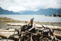 a woman sitting on driftwood on a shore 