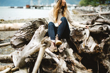 a woman sitting on a pile of driftwood 