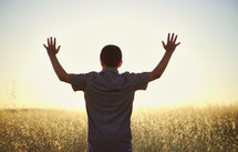 a young man with raised hands standing in a field 