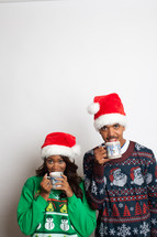 couple in ugly Christmas sweaters and santa hats sipping hot cocoa 