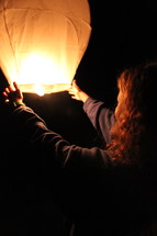 a woman lighting a floating paper lantern 