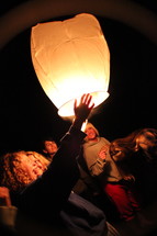 friends lighting a floating paper lantern at night 