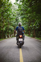 man riding a motorcycle on the center lines of a road 