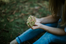teen girl sitting in grass holding picked flowers 