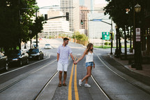 A young man and woman holding hands and walking together down a city street.
