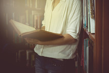 a woman standing in a library reading a book 