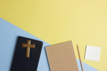 cross, BIble, and notebook on a pink and yellow background 