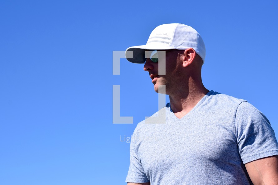 side profile of a man in a ball cap standing against a blue sky in summer 