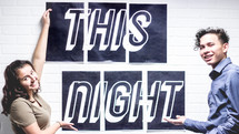 teens pointing to a poster that reads This Night 