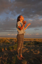 a teen girl with raised hands standing in a field 