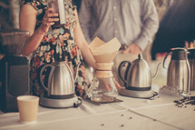 People standing near coffee urns on a table.