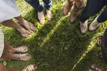 Circle of women's feet standing in the grass.