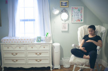 a pregnant woman holding her belly sitting in a rocking chair in a nursery 