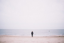 A young woman standing at the edge of the ocean on a beach.