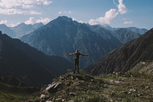 a man with outstretched arms and mountain peaks 