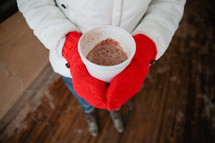 woman in mittens holding a cup of hot cocoa 