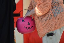 a woman holding a jack-o-lantern Halloween bucket passing out candy 