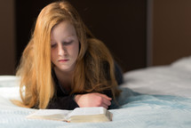a teen girl reading a Bible on a bed 