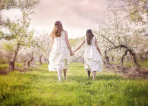 sisters walking holding hands outdoors in dresses 