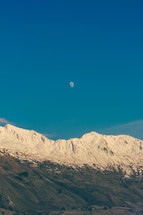 moon above snow capped mountain peaks 