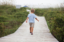 Boy walking on a boardwalk at the beach.