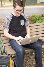 a college student sitting on bench with his laptop 