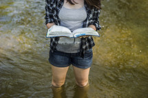 woman standing in knee high water reading a Bible